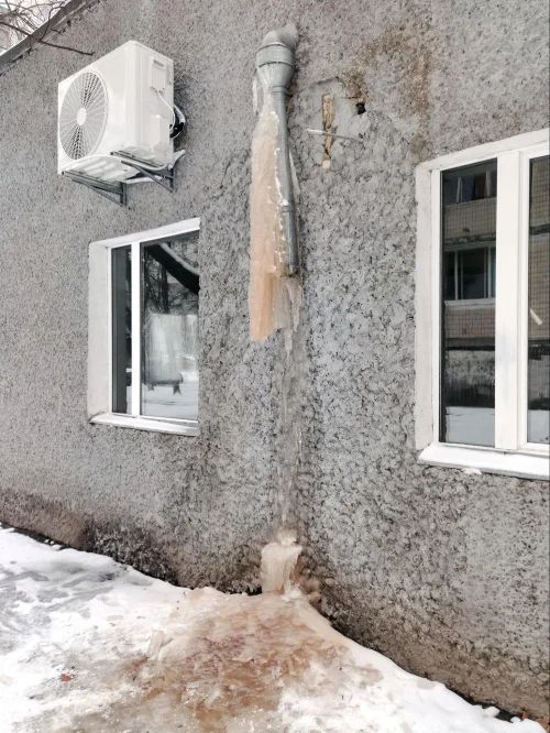 Heavy ice buildup around a drainpipe on a damaged stucco wall